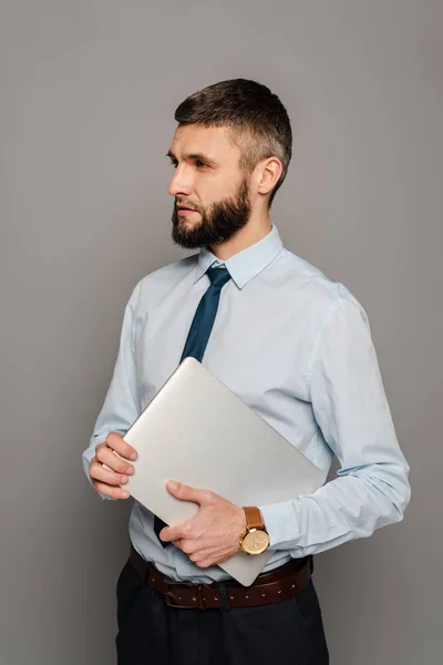 Handsome bearded businessman with laptop on grey background — Stock Photo