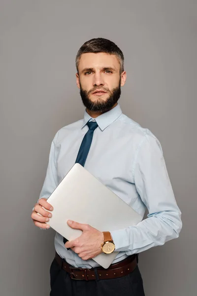 Handsome bearded businessman with laptop on grey background — Stock Photo