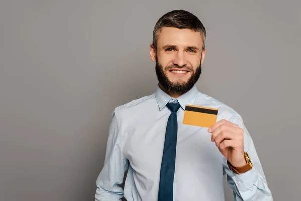 Усміхнений красивий бородатий бізнесмен з кредитною карткою на сірому фоні — стокове фото