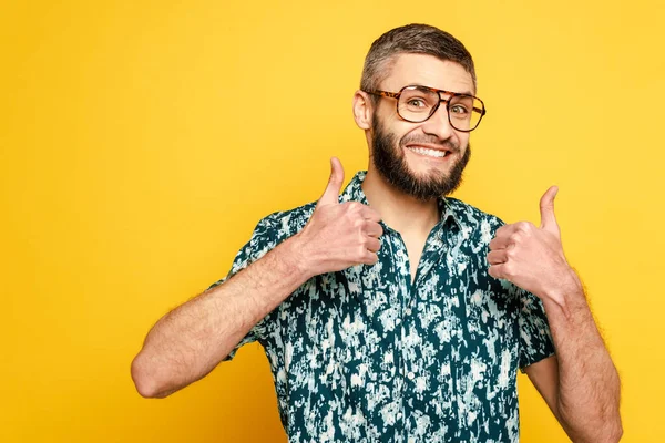 Sourire barbu gars dans des lunettes montrant pouces vers le haut sur jaune — Photo de stock