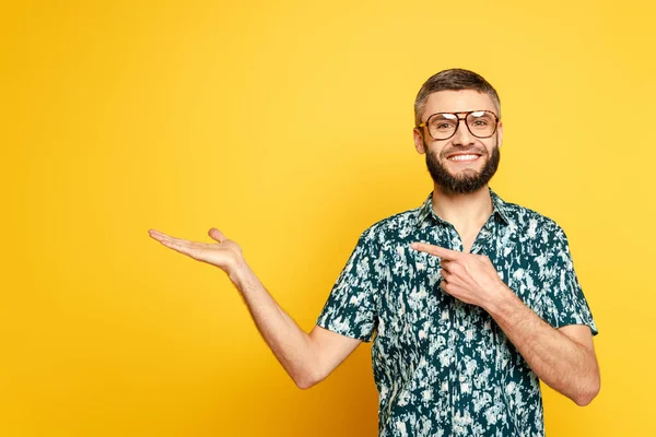 Sourire barbu gars dans des lunettes pointant avec le doigt de côté sur jaune — Photo de stock