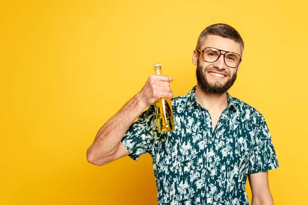 Ragazzo barbuto sorridente in bicchieri con bottiglia di birra su giallo — Foto stock