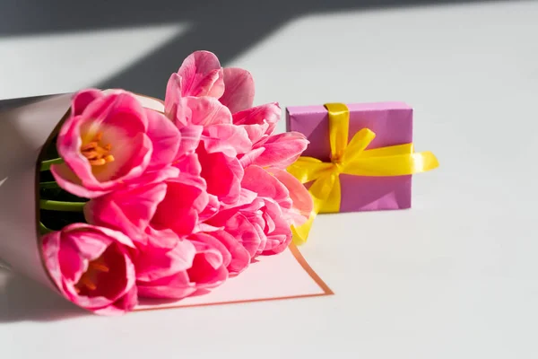 Ramo de tulipanes rosados cerca de una pequeña caja de regalo en blanco, concepto de día de la madre - foto de stock