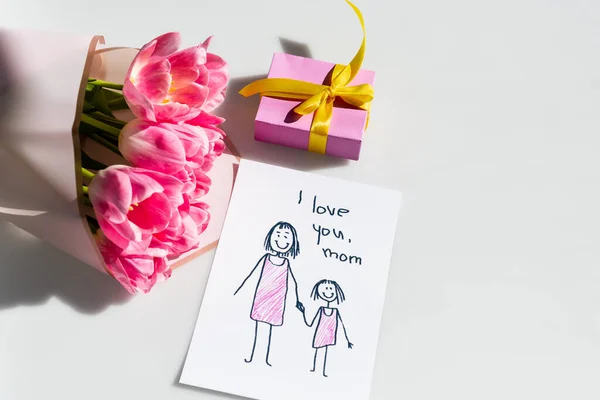 Ramo de tulipanes cerca de la pequeña caja de regalo y tarjeta de felicitación con te amo mamá letras en blanco - foto de stock