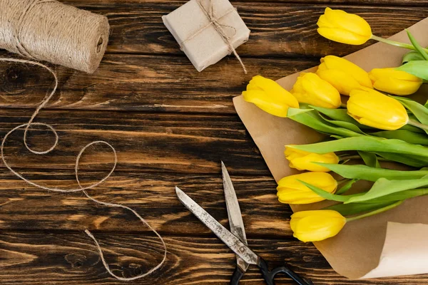 Top view of yellow tulips near scissors, jute twine rope and gift box on wooden surface, mothers day concept — Stock Photo