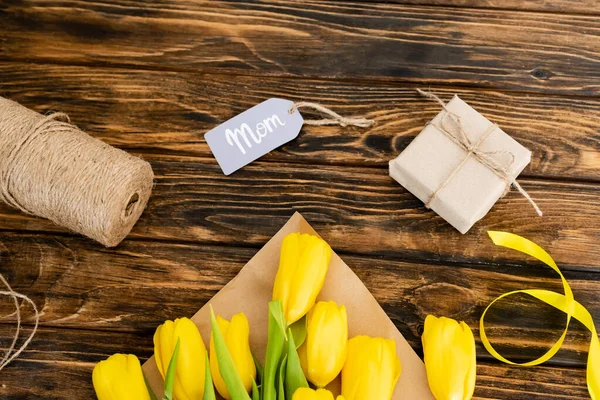 Vue du dessus des tulipes jaunes près de corde de ficelle de jute et boîte cadeau avec lettrage maman sur l'étiquette, concept de fête des mères — Photo de stock