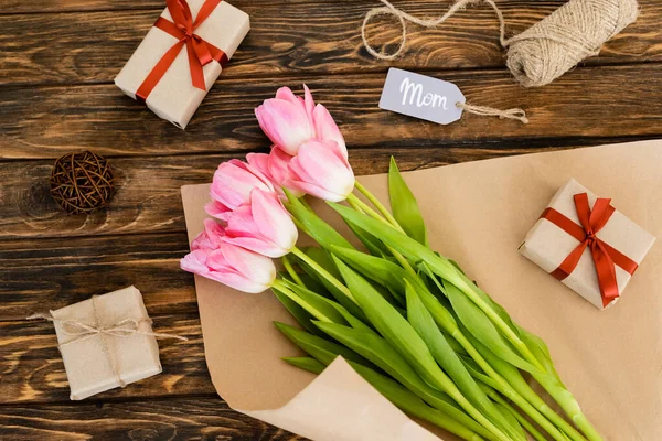 Vista superior de la etiqueta con letras de mamá cerca de regalos y tulipanes en la superficie de madera, concepto de día de las madres - foto de stock