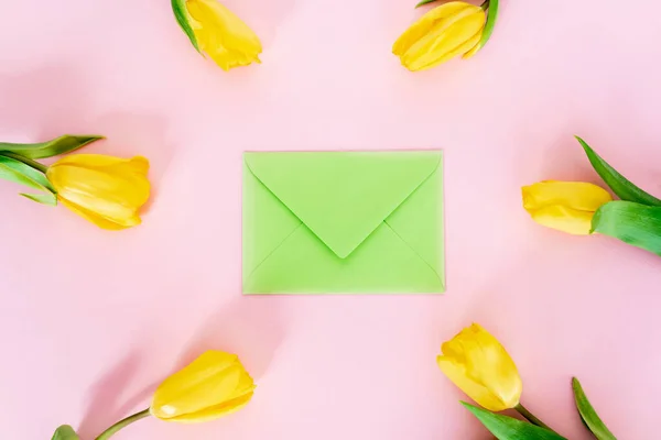 Top view of green envelope near yellow tulips on pink, mothers day concept — Stock Photo