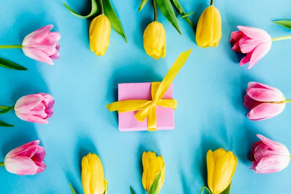 Top view of blooming yellow and pink tulips near gift box on blue, mothers day concept — Stock Photo