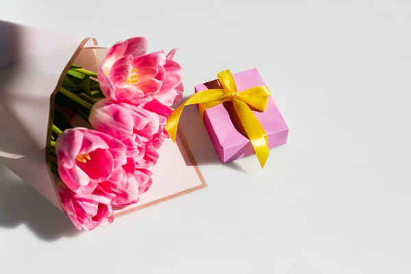 Sunlight on pink tulips near gift box on white, mothers day concept — Stock Photo