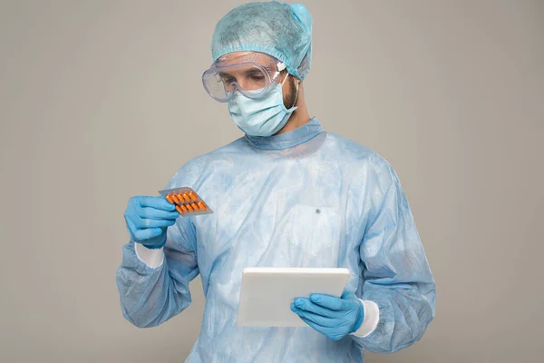 Medico in maschera medica con blister con pillole e tablet digitale isolato su grigio — Foto stock