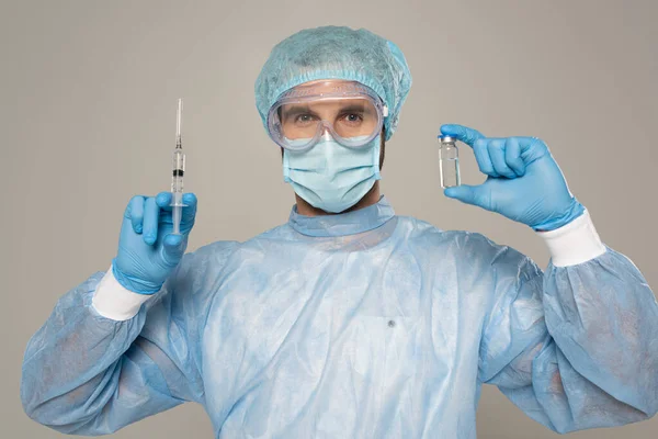 Лікар в захисних окулярах і медичній масці тримає шприц і банку вакцини ізольовані на сірому — стокове фото