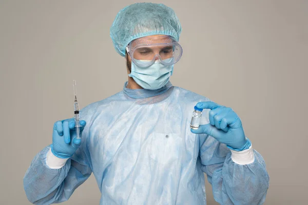 Doctor in medical mask and protective googles holding jar of vaccine and syringe isolated on grey — Stock Photo