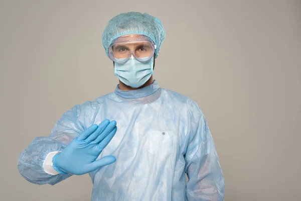 Doctor en máscara médica mostrando gesto de stop en cámara aislada en gris - foto de stock