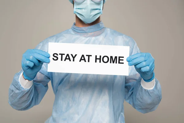 Vista recortada de la tarjeta de retención del médico con letras de estancia en casa aisladas en gris - foto de stock