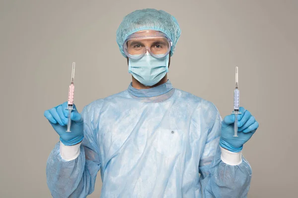 Лікар в медичній масці та захисних окулярах тримає шприци з вакциною ізольовані на сірому — стокове фото