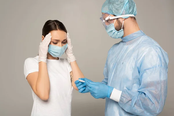 Médecin tenant thermomètre près inquiet patient isolé sur gris — Photo de stock