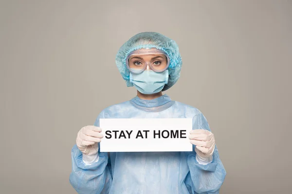 Médico em óculos de proteção e cartão de segurança máscara médica com estadia em casa lettering isolado em cinza — Fotografia de Stock