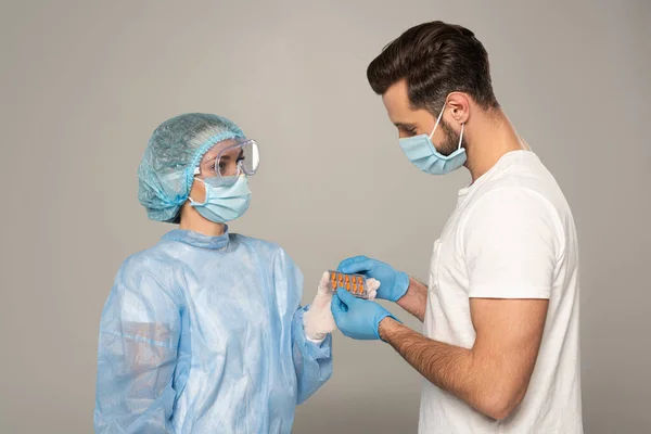 Side view of doctor giving blister with pills at patient isolated on grey — Stock Photo