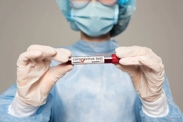 Vista recortada del médico sosteniendo el tubo de ensayo con muestra de sangre y letras de coronavirus aisladas en gris - foto de stock