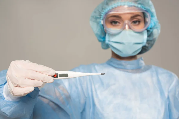 Selective focus of doctor in safety googles holding thermometer isolated on grey — Stock Photo