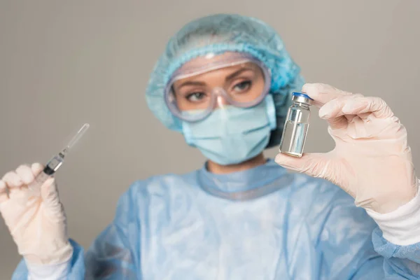 Focus selettivo del medico in maschera medica e tappo contenente siringa e vasetto di vaccino isolato su grigio — Foto stock