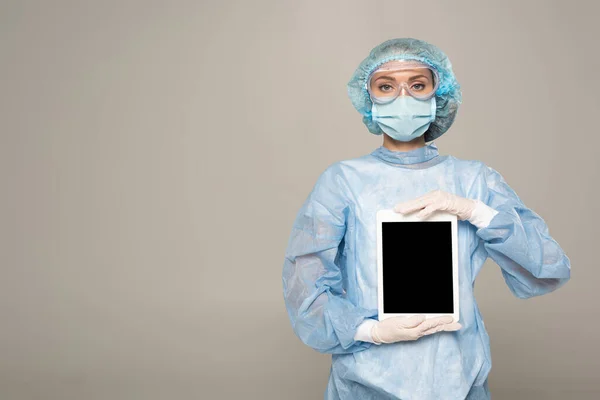 Arzt mit Schutzbrille und medizinischer Maske hält digitales Tablet mit leerem Bildschirm isoliert auf grau — Stockfoto