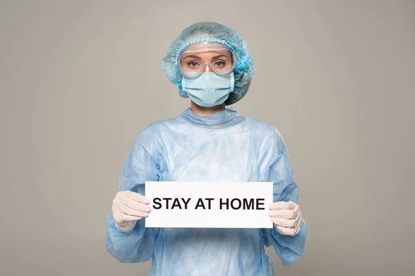 Médico em máscara médica e cartão de segurança tampa com estadia em casa lettering isolado em cinza — Fotografia de Stock