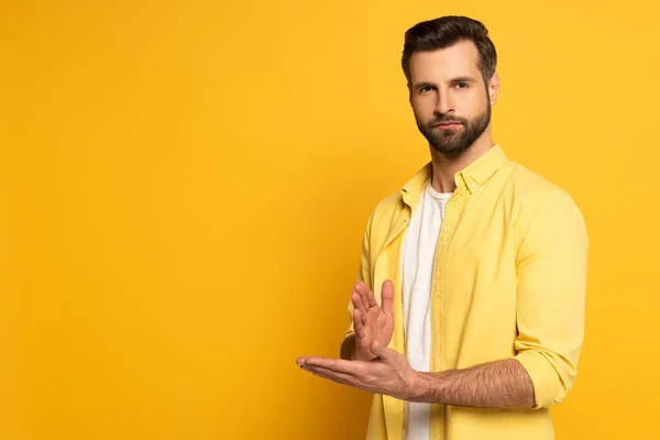 Jeune homme regardant la caméra tout en montrant le geste dans un langage sourd et muet sur fond jaune — Photo de stock