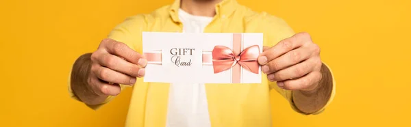 Vista recortada del hombre sosteniendo tarjeta de regalo sobre fondo amarillo, plano panorámico - foto de stock