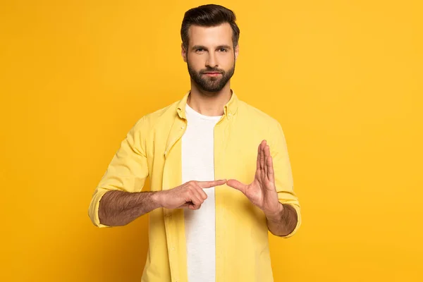 Uomo guardando la fotocamera mentre mostra il gesto dal linguaggio dei segni su sfondo giallo — Foto stock