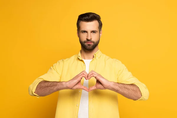 Schöner Mann zeigt Liebeszeichen auf gelbem Hintergrund — Stockfoto