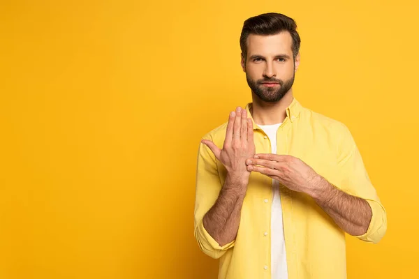 Uomo che mostra gesto dal linguaggio dei segni su sfondo giallo — Foto stock
