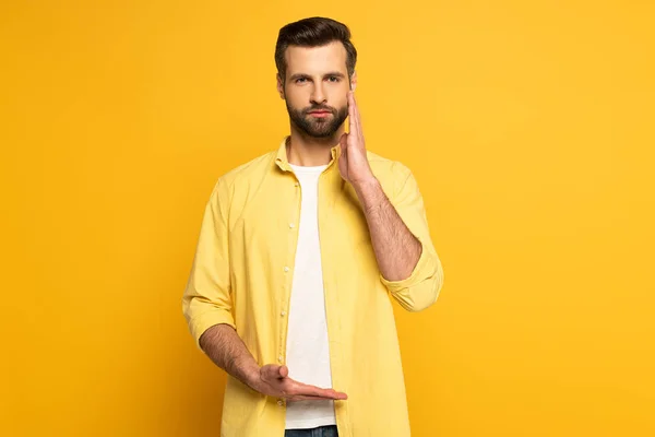 Hombre mirando a la cámara mientras usa el gesto del lenguaje de señas sobre fondo amarillo - foto de stock