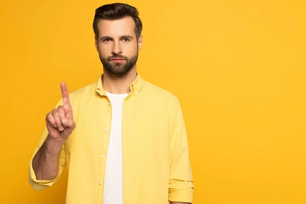 Hombre guapo apuntando hacia arriba con el dedo y mirando a la cámara en el fondo amarillo - foto de stock