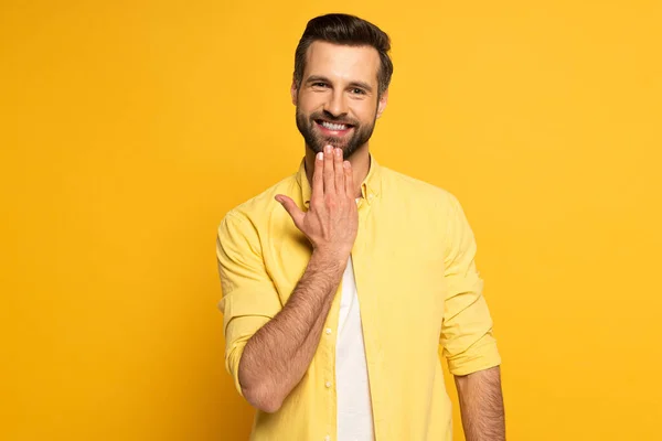 Sorrindo homem olhando para a câmera ao mostrar palavra falar em língua de sinais no fundo amarelo — Fotografia de Stock