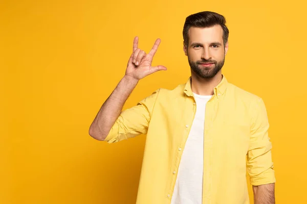 Handsome man showing word love in sign language on yellow background — Stock Photo