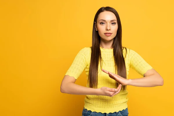 Jeune femme gestuelle tout en utilisant le langage des signes sur fond jaune — Photo de stock