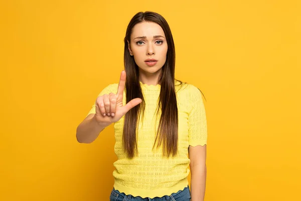 Sad woman pointing with finger and looking at camera on yellow background — Stock Photo