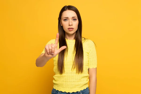 Mulher triste apontando com o dedo e olhando para a câmera no fundo amarelo — Fotografia de Stock