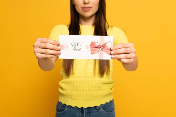 Vista recortada de la mujer que muestra la tarjeta de regalo sobre fondo amarillo - foto de stock