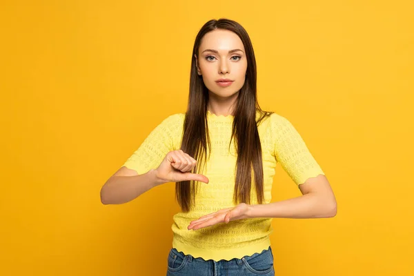 Hermosa mujer haciendo gestos mientras usa lenguaje de señas sobre fondo amarillo - foto de stock