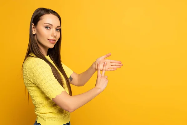 Visão lateral da mulher mostrando gesto em linguagem surda e muda em fundo amarelo — Fotografia de Stock