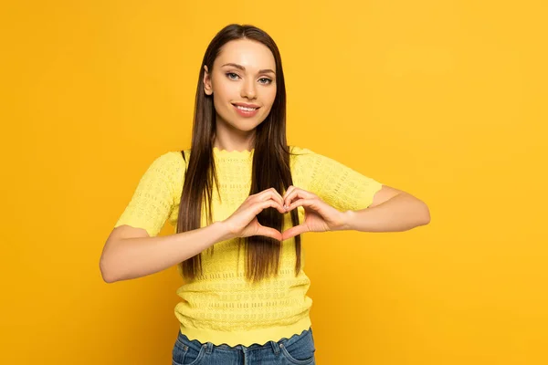 Beautiful smiling woman showing heart sign on yellow background — Stock Photo