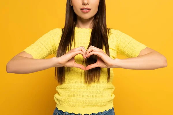 Vista ritagliata della donna che mostra segno d'amore su sfondo giallo — Foto stock