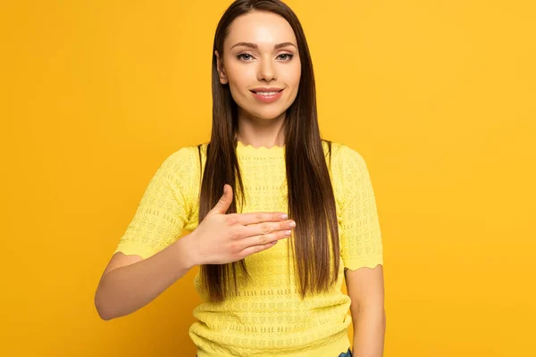 Smiling woman looking at camera while using sign language on yellow background — Stock Photo