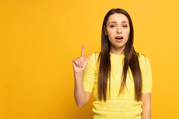 Esistito ragazza che punta con il dito e guardando la fotocamera su sfondo giallo — Foto stock