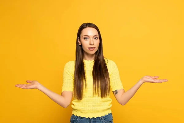 Fille attrayante montrant geste haussant les épaules sur fond jaune — Photo de stock