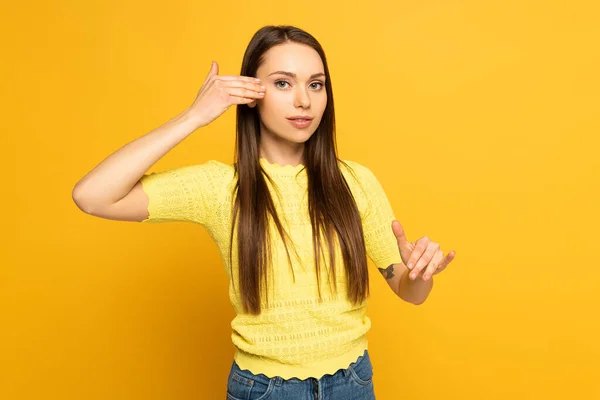 Mujer joven haciendo gestos mientras usa lenguaje sordo y mudo sobre fondo amarillo - foto de stock