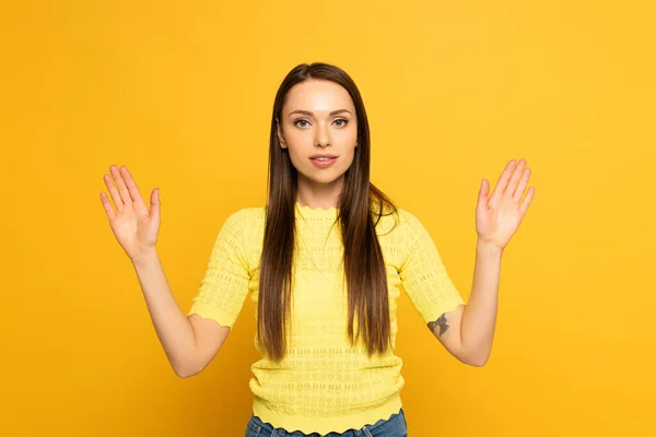 Mujer joven mirando a la cámara mientras usa lenguaje de señas sobre fondo amarillo - foto de stock